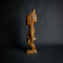 Load image into Gallery viewer, Hand-carved wooden statue of a mother holding a child, embodying fertility and continuity in African culture.