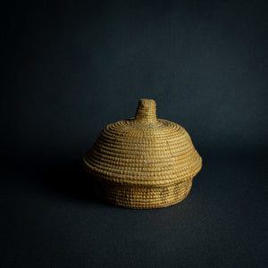 Handwoven African basket with a conical lid on a dark background.