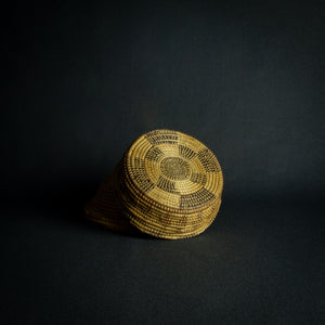 Handwoven African basket with a conical lid on a dark background.