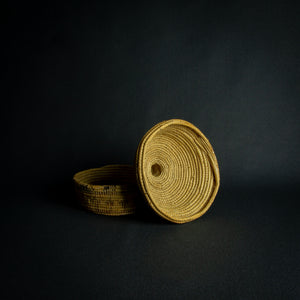 Handwoven African basket with a conical lid on a dark background.