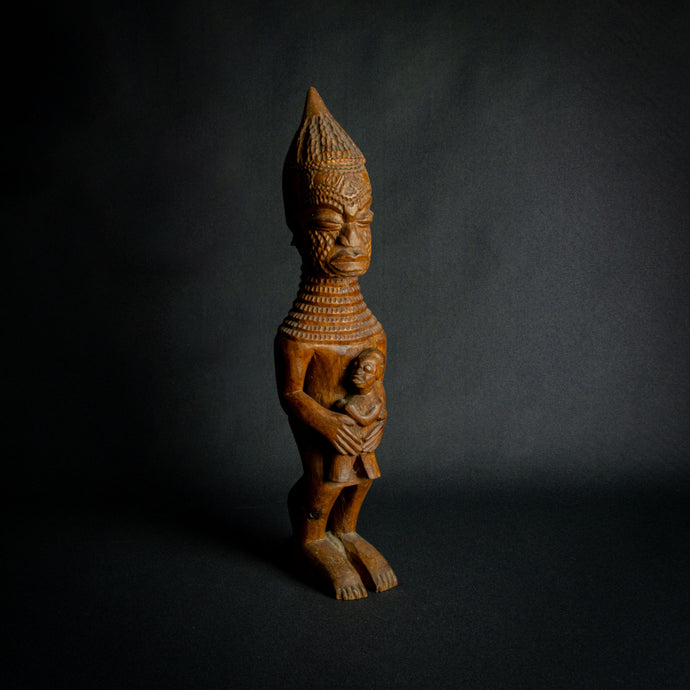 Hand-carved wooden statue of a mother holding a child, embodying fertility and continuity in African culture.