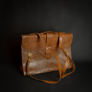 Vintage brown embossed leather briefcase with gold-tone hardware on a dark background.