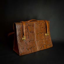 Load image into Gallery viewer, Vintage brown embossed leather briefcase with gold-tone hardware on a dark background.
