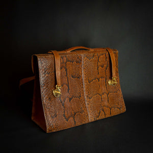 Vintage brown embossed leather briefcase with gold-tone hardware on a dark background.