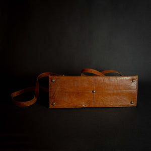 Vintage brown embossed leather briefcase with gold-tone hardware on a dark background.