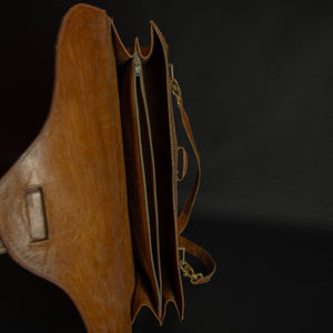 Vintage brown embossed leather briefcase with gold-tone hardware on a dark background.