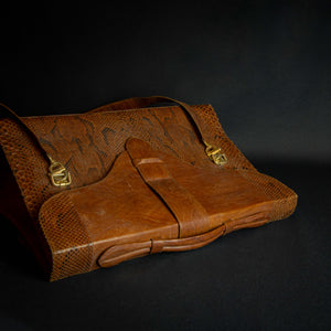 Vintage brown embossed leather briefcase with gold-tone hardware on a dark background.