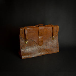 Vintage brown embossed leather briefcase with gold-tone hardware on a dark background.